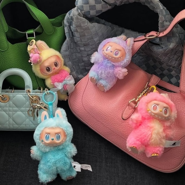 Four pastel-colored Labubu plush keychains with large eyes and animal ears are attached to green, gray, pink, and light blue handbags displayed against a dark background—can you guess your favorite in this fun quiz of style?.