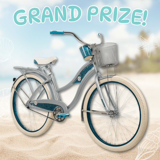 A teal and silver Huffy Beach Cruiser with a basket stands on sandy beach, the blurred sea and sky in the background. Text above reads GRAND PRIZE! with playful seashell and starfish illustrations.